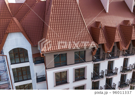 Close-up of building facade exterior with stucco wall, cast iron balcony railings, steep shingle roof and shiny windows. Close-up of building facade exterior with stucco wall, cast iron balcony railings, steep shingle roof and shiny windows. 96011337