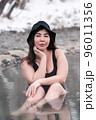 Overweight young woman with big breast in black one-piece bathing swimsuit costume, panama hat sitting in outdoors pool at spa resort. Plus size busty female looking at camera. Body positive concept 96011356