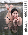 Plus size model in bathing suit lying down in geothermal mineral water in outdoor pool at balneotherapy health spa, hot springs resort having balneological properties. Woman looking at camera, smiling 96011364