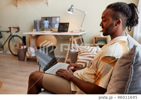 Man using laptop while sitting on sofa and smiling 96011695