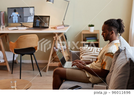 Black man using laptop while sitting on sofa 96011696