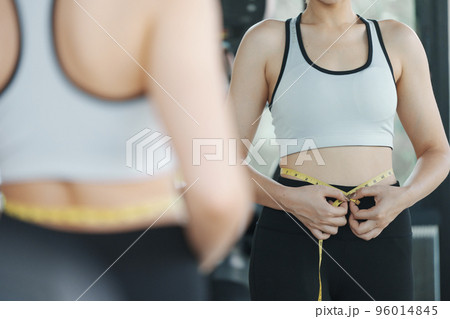 Young woman measuring her waist by measure tape at the gym. 96014845