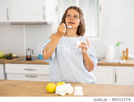 Young woman eating tasty yogurt in kitchen Young woman eating tasty yogurt in kitchen 96015278