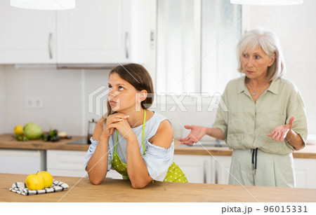 Upset girl at home kitchen while worried elderly mother reprimanding her. Family conflicts concept 96015331