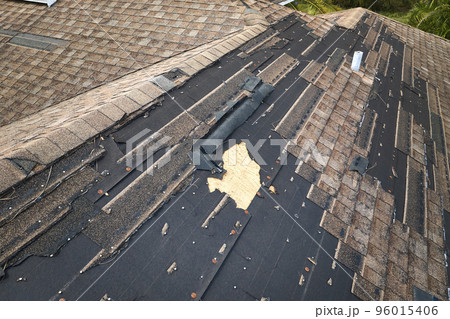 Wind damaged house roof with missing asphalt shingles after hurricane Ian in Florida. Repair of home rooftop concept Wind damaged house roof with missing asphalt shingles after hurricane Ian in Florida. Repair of home rooftop concept 96015406
