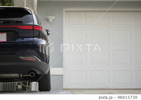 Car parked in front of wide garage double door on concrete driveway of new modern american house Car parked in front of wide garage double door on concrete driveway of new modern american house 96015730