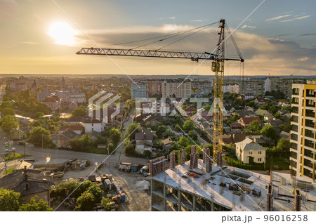 Apartment or office tall building under construction. Brick walls, glass windows, scaffolding and concrete support pillars. Tower crane on bright blue sky copy space background. 96016258