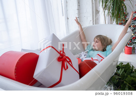 A teenage girl is taking a bath. The bathtub is filled with gift boxes. Merry christmas concept. A teenage girl is taking a bath. The bathtub is filled with gift boxes. Merry christmas concept. 96019308