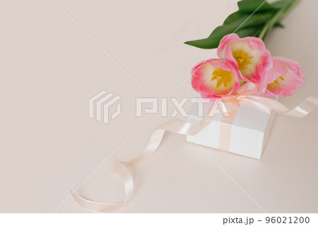 A bouquet of beautiful tulips and a gift on a beige background top view. Mother's Day Background, Valentine Day, International Women's Day. Holiday, give a gift. 96021200