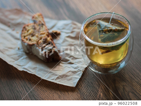 Herbal tea in glass and biscuit on craft paper. Cozy breakfast. Tea bag in glass with cake. Hot drink and dessert. Fresh bakery and tea in cafe.  96022508