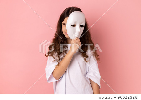 Portrait of dark haired little girl wearing white T-shirt covering face, standing with frowning face, multiple personality disorder. Indoor studio shot isolated on pink background. 96022928