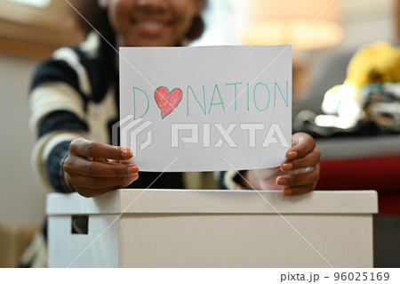 Young woman hands holding paper with donate label and smiling at camera. Charity, donation and reuse recycle concept Young woman hands holding paper with donate label and smiling at camera. Charity, donation and reuse recycle concept 96025169