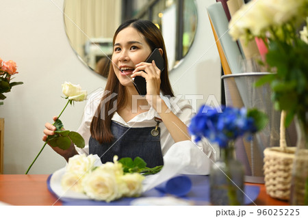 Beautiful young asian woman talking on mobile phone, taking orders from clients while sitting in her floral shop Beautiful young asian woman talking on mobile phone, taking orders from clients while sitting in her floral shop 96025225