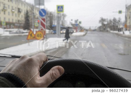 driver hand behind the wheel of a car that gives way to a pedestrian at a pedestrian crossing 96027439