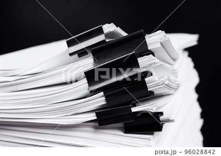 A stack of office papers, some of which are fastened with black binders 96028842