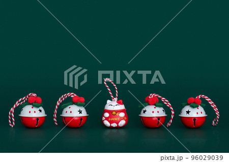 Christmas bells and Lucky cat figure in a row on green background. Christmas theme. Four beautiful red-white decorating jingle bells with swirl ribbons and red-white Lucky cat between them. 96029039