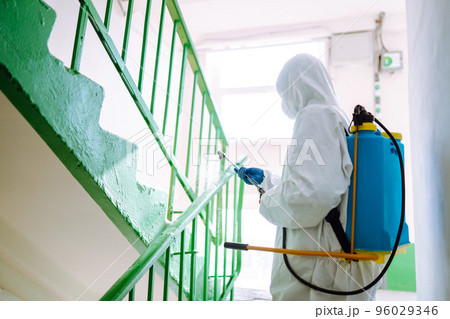 Man in Hazmat suit, protective gloves and goggles use sprayer equipment disinfect the entrance. Man in Hazmat suit, protective gloves and goggles use sprayer equipment disinfect the entrance. 96029346