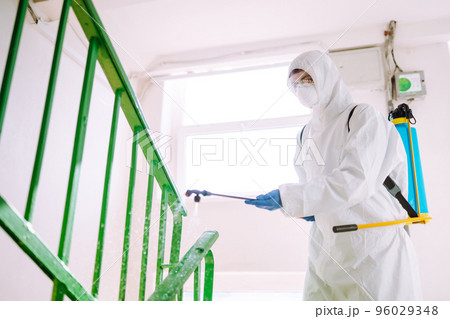 Man in Hazmat suit, protective gloves and goggles use sprayer equipment disinfect the entrance. Man in Hazmat suit, protective gloves and goggles use sprayer equipment disinfect the entrance. 96029348