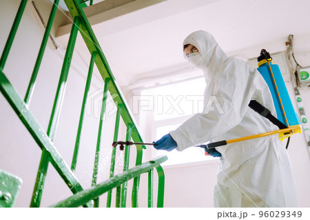 Man in Hazmat suit, protective gloves and goggles use sprayer equipment disinfect the entrance. Man in Hazmat suit, protective gloves and goggles use sprayer equipment disinfect the entrance. 96029349