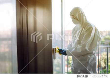 Cleaning and disinfection of the elevator to prevent COVID-19. Worker wearing protective suit sprays. 96029370