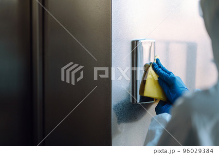 Cleaning and disinfection of the elevator to prevent COVID-19. Worker wearing protective suit sprays. 96029384