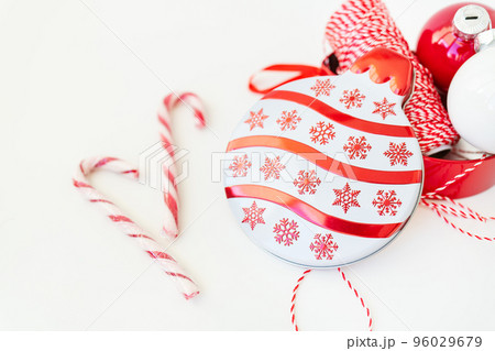 Christmas candies, along with toys for the Christmas tree and a red thread for wrapping gifts, lie on a white table. Selective focus, noise. Christmas and New Year 2023-2024. 96029679