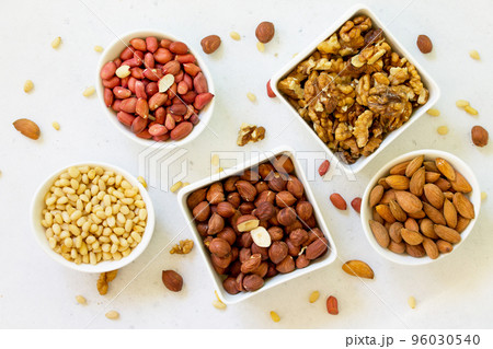 Various nuts in a ceramic bowl (walnut, almonds, pine nuts, hazelnuts) on a light stone table. The concept of a healthy dessert. Various nuts in a ceramic bowl (walnut, almonds, pine nuts, hazelnuts) on a light stone table. The concept of a healthy dessert. 96030540