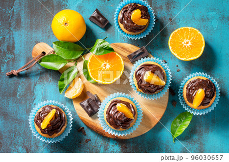 Orange Cupcakes with Chocolate Cream and Fresh Tangerines on a blue stone or concrete table. Top view flat lay background. 96030657