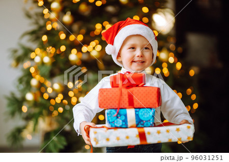 Happy child in Santa red hat receives Christmas gifts.Boy posing with present in Christmas interior Happy child in Santa red hat receives Christmas gifts.Boy posing with present in Christmas interior 96031251