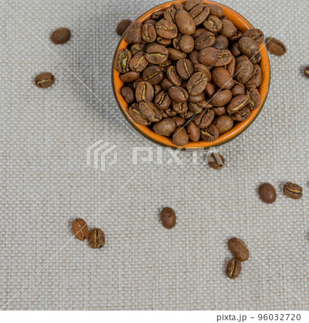 A cup with coffee beans on the background, spilled coffee beans near the cup. 96032720