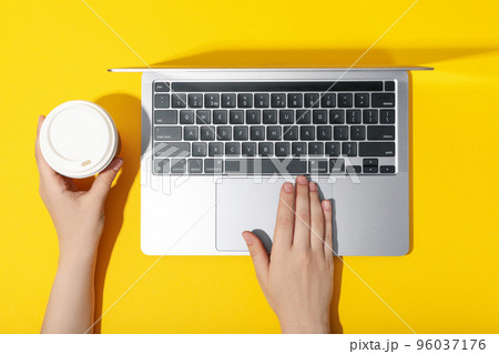 Female hands with paper cup on laptop on yellow background 96037176