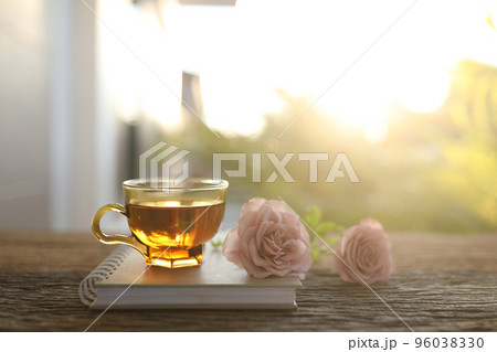 Tea glass cup and pink roses head under sunlight on wooden table Tea glass cup and pink roses head under sunlight on wooden table 96038330