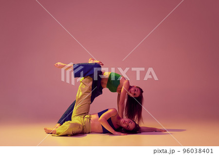 Energetic dancers in art performance at dance hall. Young stylish fashionable girls dancing isolated on crystal pink background. Art, fashion, style Energetic dancers in art performance at dance hall. Young stylish fashionable girls dancing isolated on crystal pink background. Art, fashion, style 96038401