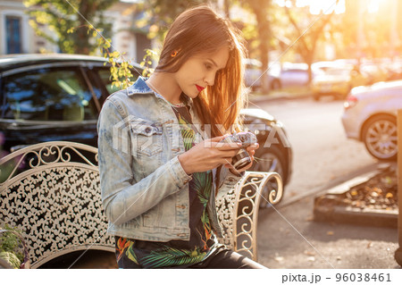 Outdoor autumn smiling lifestyle portrait of pretty young woman, having fun in the city with camera, travel photo of photographer. 96038461