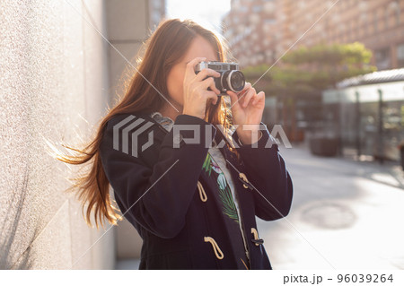 Outdoor autumn smiling lifestyle portrait of pretty young woman, having fun in the city with camera, travel photo of photographer. Outdoor autumn smiling lifestyle portrait of pretty young woman, having fun in the city with camera, travel photo of photographer. 96039264