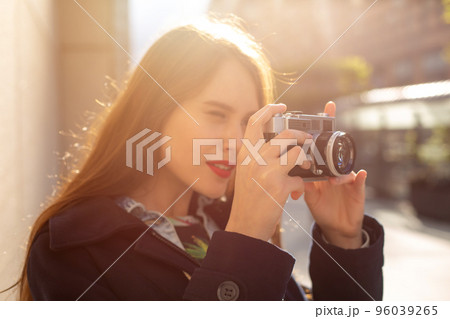 Outdoor autumn smiling lifestyle portrait of pretty young woman, having fun in the city with camera, travel photo of photographer. 96039265