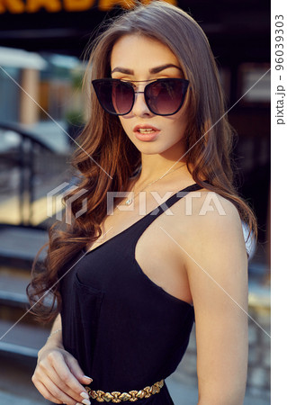 Fashion style portrait of young beautiful elegant woman in black dress walking at city streets. 96039303
