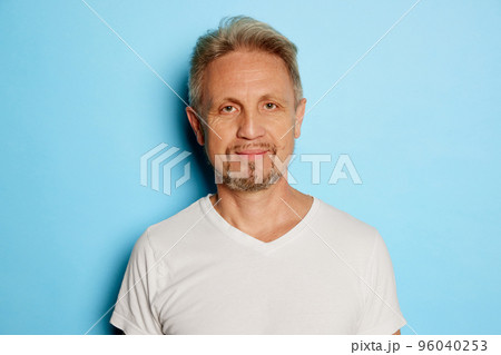 Portrait of mature man in white T-shirt posing, looking at camera isolated over blue studio background Portrait of mature man in white T-shirt posing, looking at camera isolated over blue studio background 96040253