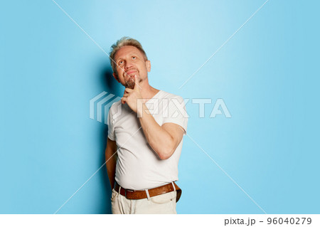 Portrait of mature man in white T-shirt posing isolated over blue studio background. Thoughful face Portrait of mature man in white T-shirt posing isolated over blue studio background. Thoughful face 96040279