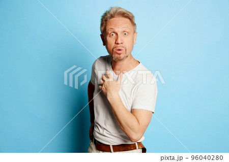 Portrait of mature man in white T-shirt posing isolated over blue studio background. Shocked face Portrait of mature man in white T-shirt posing isolated over blue studio background. Shocked face 96040280