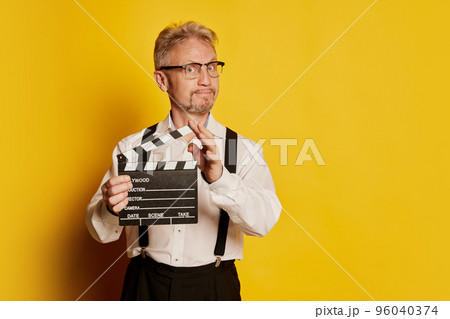 Portrait of mature man in stylish classical clothes posing isolated over yellow studio background. Movie scenario Portrait of mature man in stylish classical clothes posing isolated over yellow studio background. Movie scenario 96040374