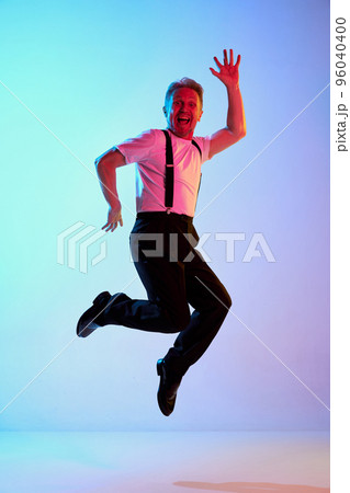 Portrait of mature man in shirt posing, cheerfully jumping isolated over gradient purple background in neon light 96040400
