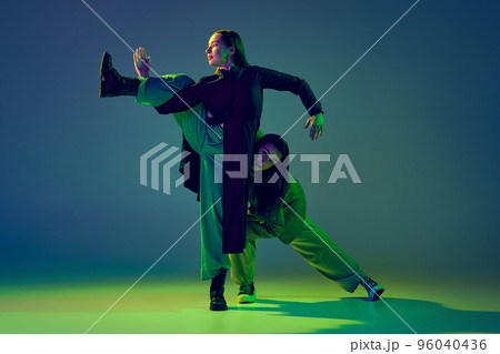 Two dancers, stylish fashionable dance couple dancing contemporary dance on colorful gradient blue-green background in neon light. Concept of art, creativity, movement, style and fashion, action. 96040436