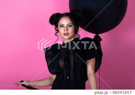 beauty portrait of a brunette girl in a black dress on a pink background with a black inflatable ball 96041857