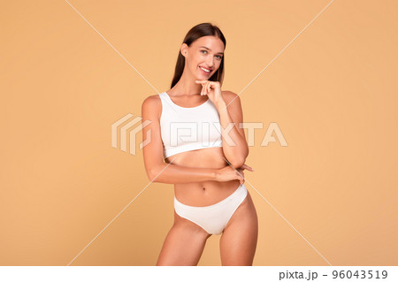 Body slimming concept. Happy caucasian woman with fit figure in white underwear smiling at camera, beige background Body slimming concept. Happy caucasian woman with fit figure in white underwear smiling at camera, beige background 96043519