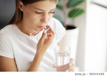 Healthy young woman holding pill glass of water Healthy young woman holding pill glass of water 96044488