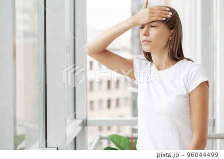 Beautiful stressed young office worker sitting at desk holding head because of pain in office 96044499