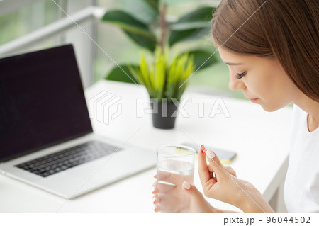 Healthy young woman holding pill glass of water Healthy young woman holding pill glass of water 96044502