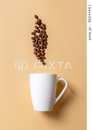 White mug and roasted coffee beans above it over beige background. 96044661