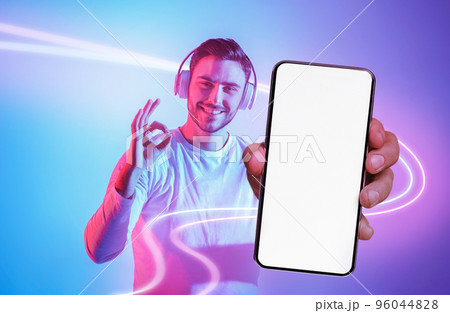 Handsome young man with headphones showing cell phone and okay 96044828